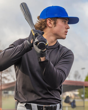 Person holding a baseball bat on a sports field with a cloudy sky.