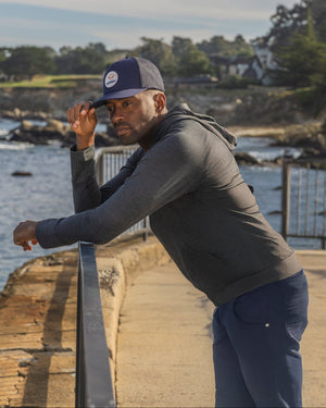 Man standing by a waterfront with trees and buildings in the background